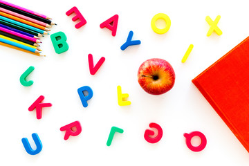 Primary school concept. Letters of english alphabet, book, apple and color pencils on white background top view