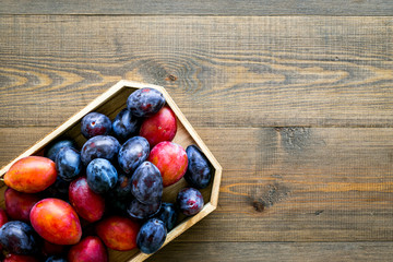 Plums on dinning table. Fresh raw red and blue plum in wooden tray on wooden background top view copy space