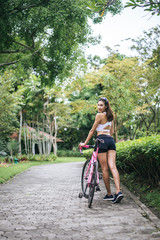 Portrait of young beautiful woman with pink bike in the park. Actractive healthy woman.