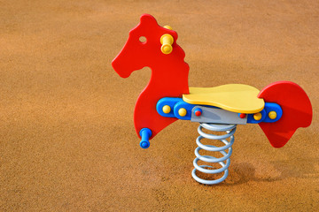 Colorful swing in shape of horse for children in playground on rubber flooring background with copy...