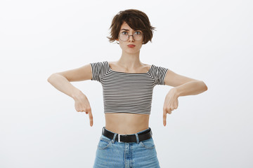 Girl came home blaming dog for spoiling her shoes. Portrait of displeased sulking cute woman in round glasses and trendy cropped top, pointing down and pouting, being displeased or offended