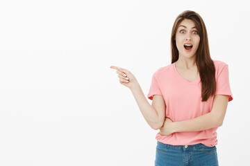 Portrait of surprised happy and joyful woman in pink t-shirt, dropping jaw and smiling while pointing left, being impressed and fascinated with fantastic car friend bought for girlfriend