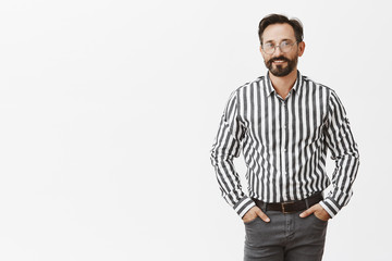 Fototapeta premium Successful and confident male entrepreneur in stylish outfit and glasses holding hands in pockets and smiling joyfully, giving speech in front students, teaching how to gain money and fame