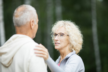 Mature blonde woman touching her husband shoulder while comforting him outdoors