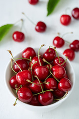 Naklejka na ściany i meble Some sweet cherries with green stems and leaves in the white ceramic bowl on the white background