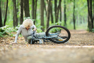 Mature active woman fell off bicycle on the ground and hurt her leg