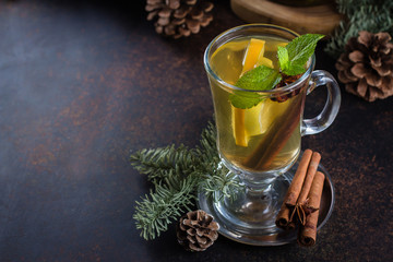 Winter Christmas Drink. Spicy citrus hot tea with ginger, cloves, cinnamon and orange slices. Warming and healthy Punch on dark background table with holiday festive decoration