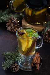Winter Christmas Drink. Spicy citrus hot tea with ginger, cloves, cinnamon and orange slices. Warming and healthy Punch on dark background table with holiday festive decoration