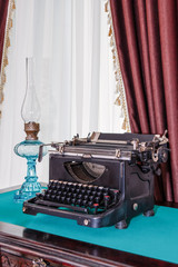 The vintage workplace of the writer with antique mechanical typewriter and the desktop kerosene lamp