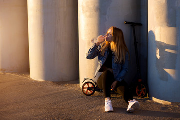 Beautiful blonde woman sitting on a scooter drinking water