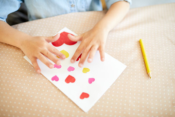 Obraz na płótnie Canvas Hands of creative little girl over handmade card with many hearts prepared for mother