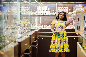 Cute small height african american girl with dreadlocks, wear at coloured yellow dress, on watches store at shopping center.