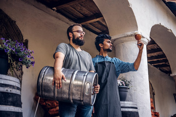 Fototapeta na wymiar Two brewers in apron standing outdoors checking the quality of brewed drink at brewery factory.