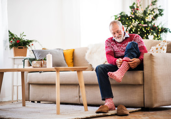A senior man putting socks on at home at Christmas time.
