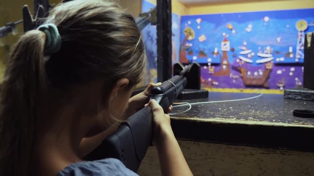 Young girl aiming with air rifle in shooting gallery. Shooting at targets in dash