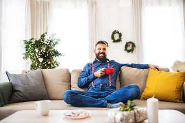 A hipster man with a red cup sitting on a sofa at home at Christmas time.