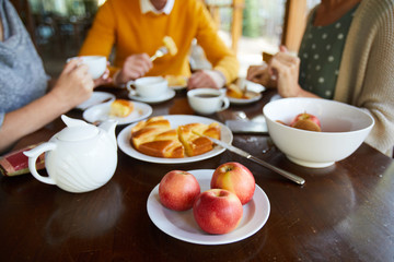 Tea party with desserts: close-up of wooden table with teapot, sweet pie and apples, friends having...