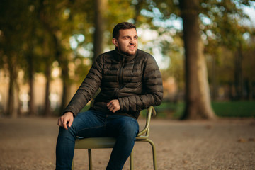Obraz premium Handsome man sits in the middle of the park in khaki stool