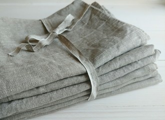 Pile of natural linen towels, napkins on white wooden background.