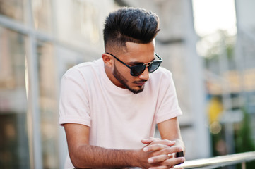 Stylish indian beard man at sunglasses and pink t-shirt. India model posed outdoor at streets of city.