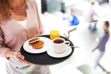 Close-up of unrecognizable waitress carrying tray with breakfast consisting of pancakes