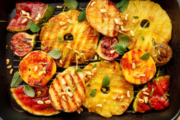 Grilled fruit; pineapples, peaches, figs, pears and watermelon with pine nuts, fresh herbs and honey on the grill plate, top view. Gourmet fruit dessert