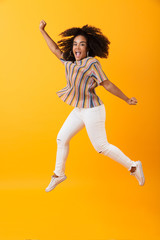 Fototapeta na wymiar Emotional pretty african woman jumping isolated over yellow background.