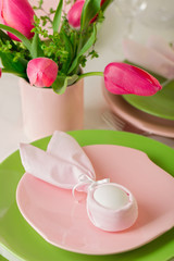 Happy easter. Decor and table setting of the Easter table is a vase with pink tulips and dishes of pink and green color.