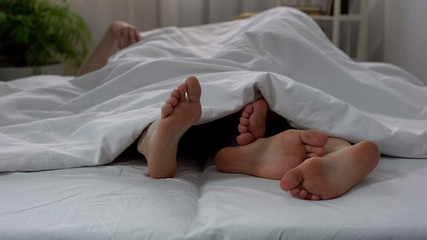 Legs of couple making love in bed seen under blanket, couple intimate relations