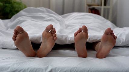 Healthy male and female feet seen under blanket, sleeping couple, skincare