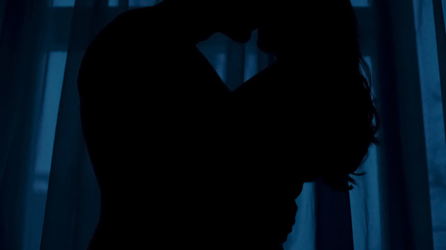 Silhouettes of young male and female hugging in dark room, love and passion