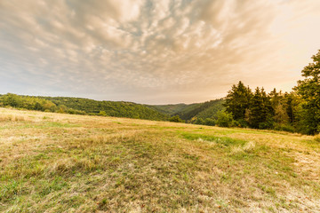 View at sunrise from top of hill as Part of Circular Hiking trail 23 Wallfhärte Weidingen near Utscheid, Eifel in Germany in dry summer or 2018 with cloudy sky