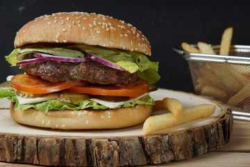 A big burger with a meat fried chop, tomatoes, pickled cucumbers, cheese, onions and salad.