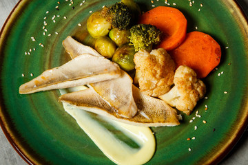 top view closeup hake fillet with vegetables and sauce served on green plate