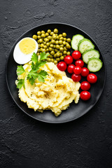 Mashed potato with green peas, tomatoes and boiled egg. Potato puree on plate with vegetables and egg