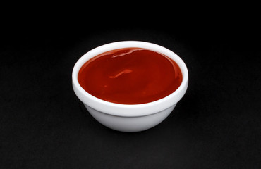 Ketchup in white bowl on black background