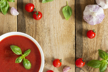 Creamy tomato soup with basil and garlic on a blue kitchen table 