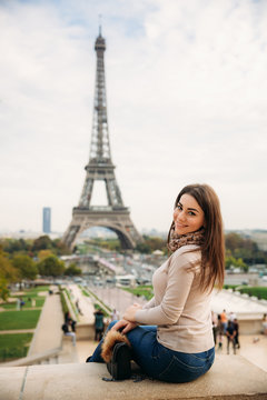 Beautiful lady sist on border against of eiffel tower. Lady smile and have fun
