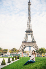 Fototapeta na wymiar Attractive young lady sist on grass. Background of eiffel tower
