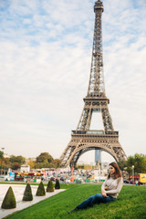 Attractive young lady sist on grass. Background of eiffel tower