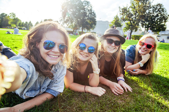 Group of happy smiling carefree young stylish woman women make friends selfie to your smartphone lying on the grass in the park, millenial concept, youth and students, tourism and holidays