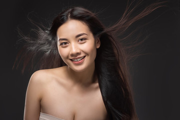 portrait of smiling asian woman with healthy and strong hair isolated on black