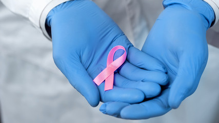 Pink ribbon in doctors hands, breast cancer awareness and prevention campaign