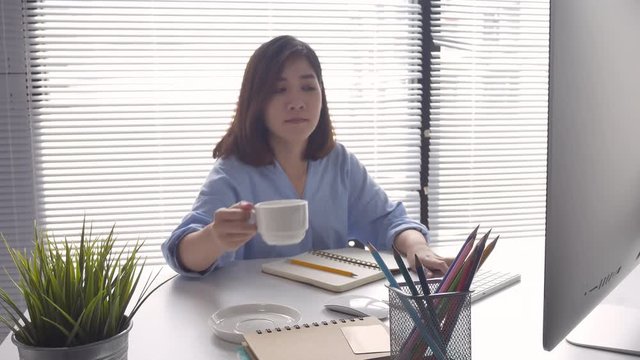 Beautiful young smiling asian woman working on computer and drinking coffee in living room at home. Asia business woman working document finance and calculator in her home office.