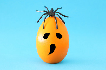 minimal and funny Halloween holiday concept. Orange egg with scary cute face and spider on top.