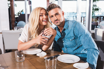 smiling couple hugging and looking at camera at table in cafe