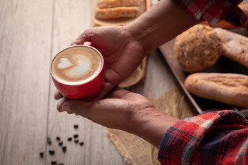 Fototapeta na wymiar Red cup of cappuccino with latte art coffee serving by hipster man hands, Coffee and breads on wooden table.