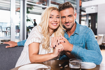 happy couple hugging and looking at camera at table in cafe