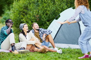Group of young friends laughing while looking at one of them during leisure game in camp