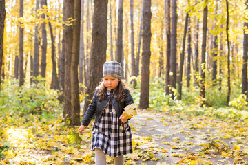 Autumn, seasons and children concept - happy little girl laughing and playing with fallen leaves in park